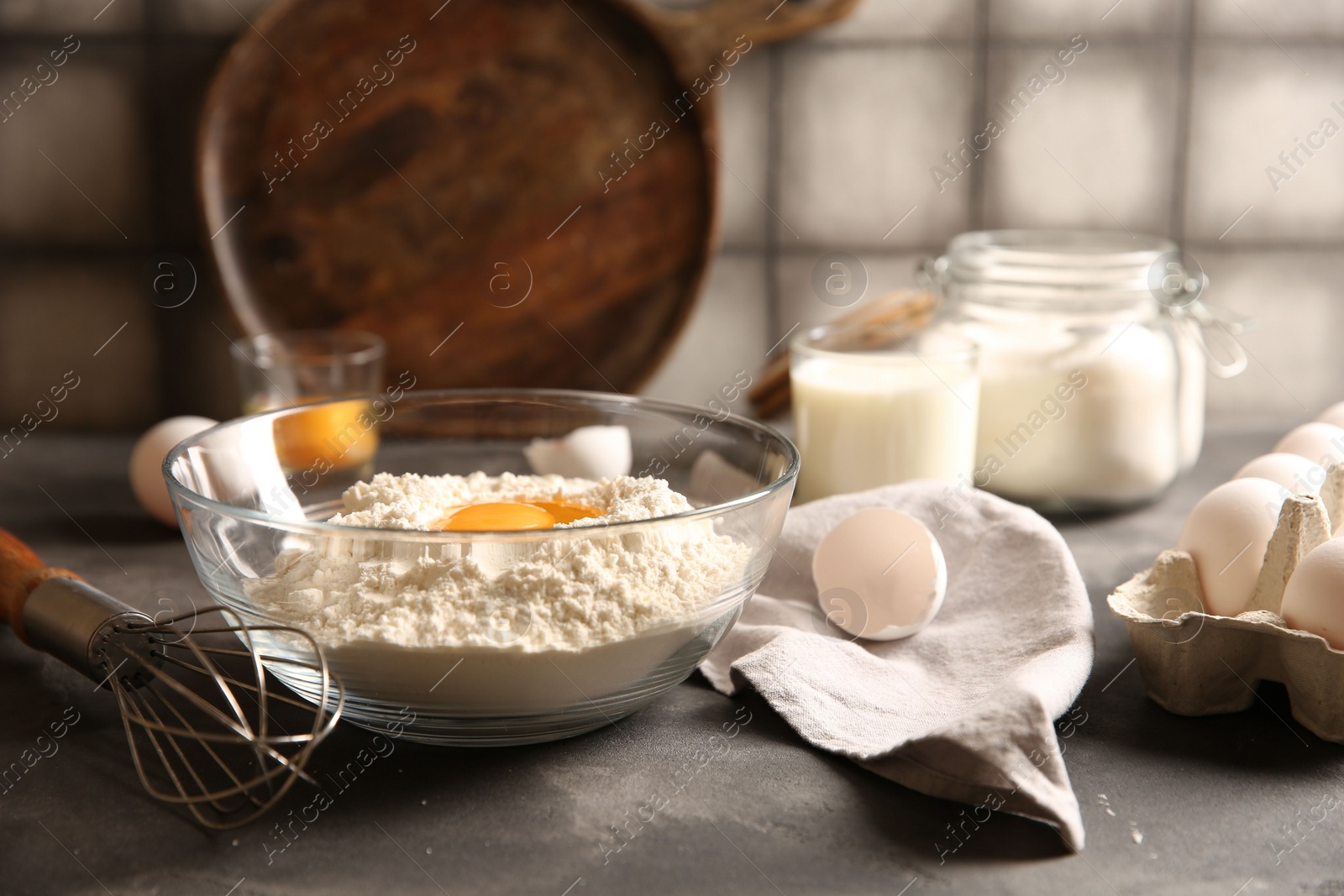 Photo of Making dough. Flour with egg yolk in bowl and whisk on grey textured table, closeup