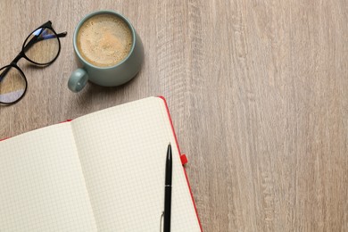 Blank notebook, cup of coffee and glasses on wooden table, flat lay. Space for text