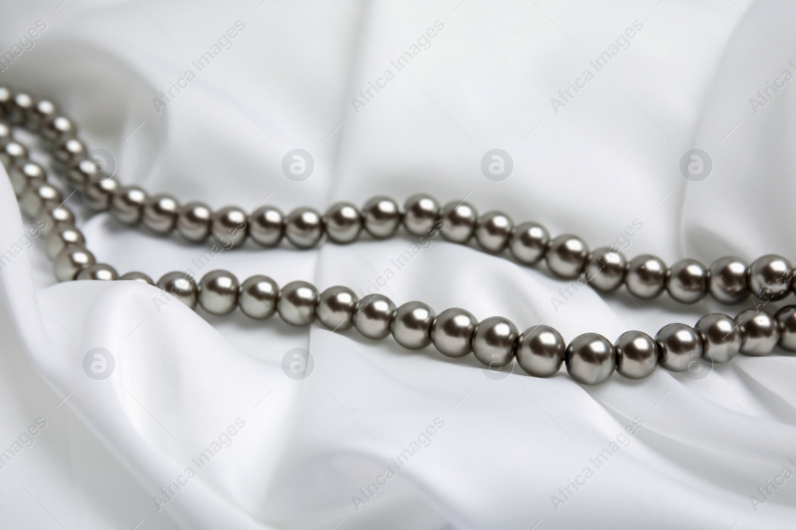 Photo of Beautiful pearls on white silk, closeup view