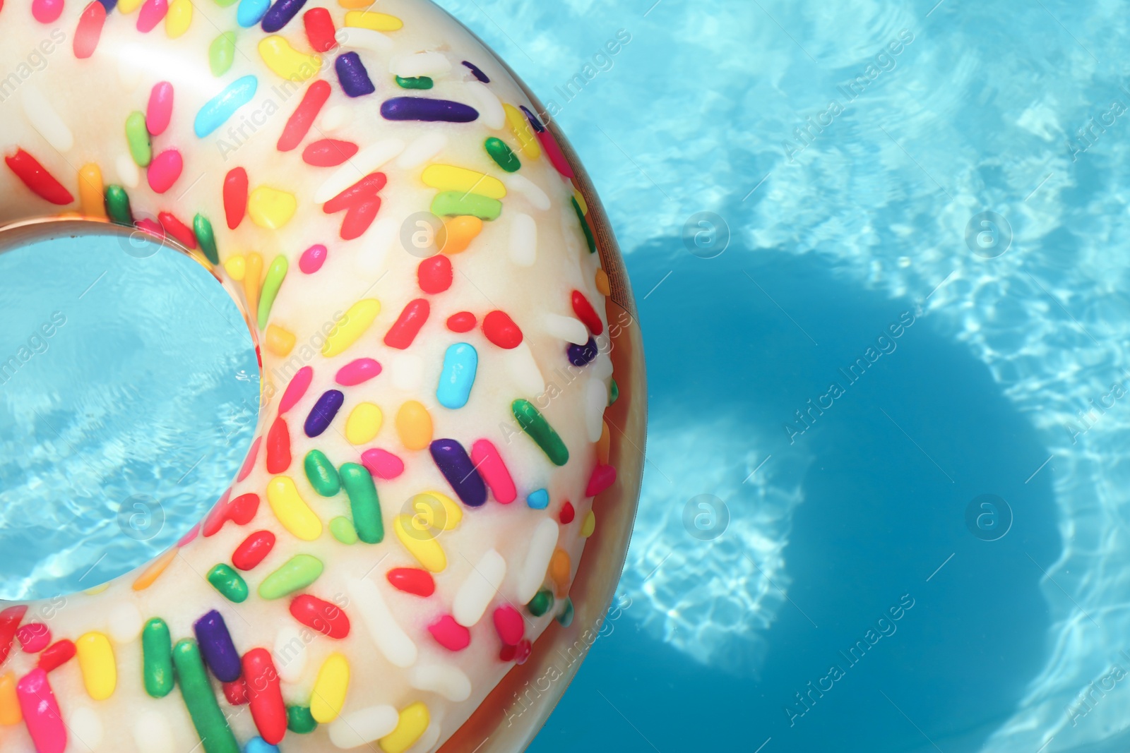 Photo of Bright inflatable doughnut ring floating in swimming pool on sunny day. Space for text