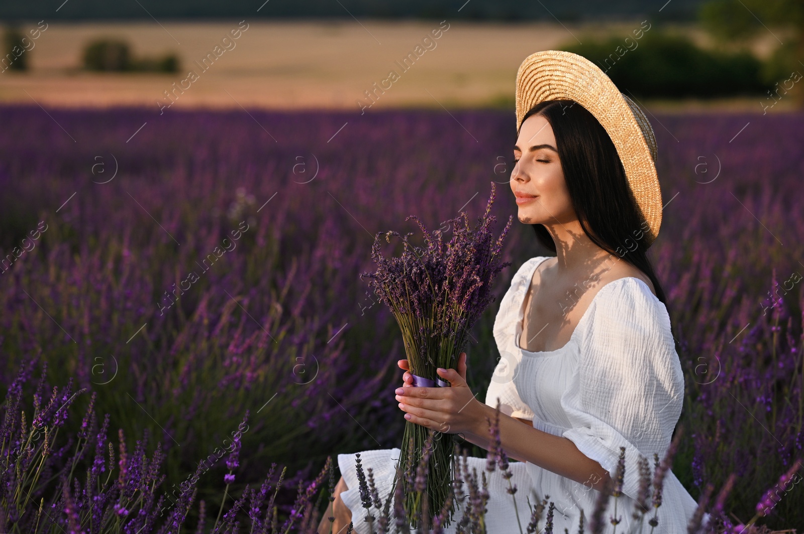 Photo of Beautiful young woman with bouquet sitting in lavender field