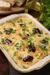 Photo of Tasty sausage casserole with green onions in baking dish on wooden table, closeup