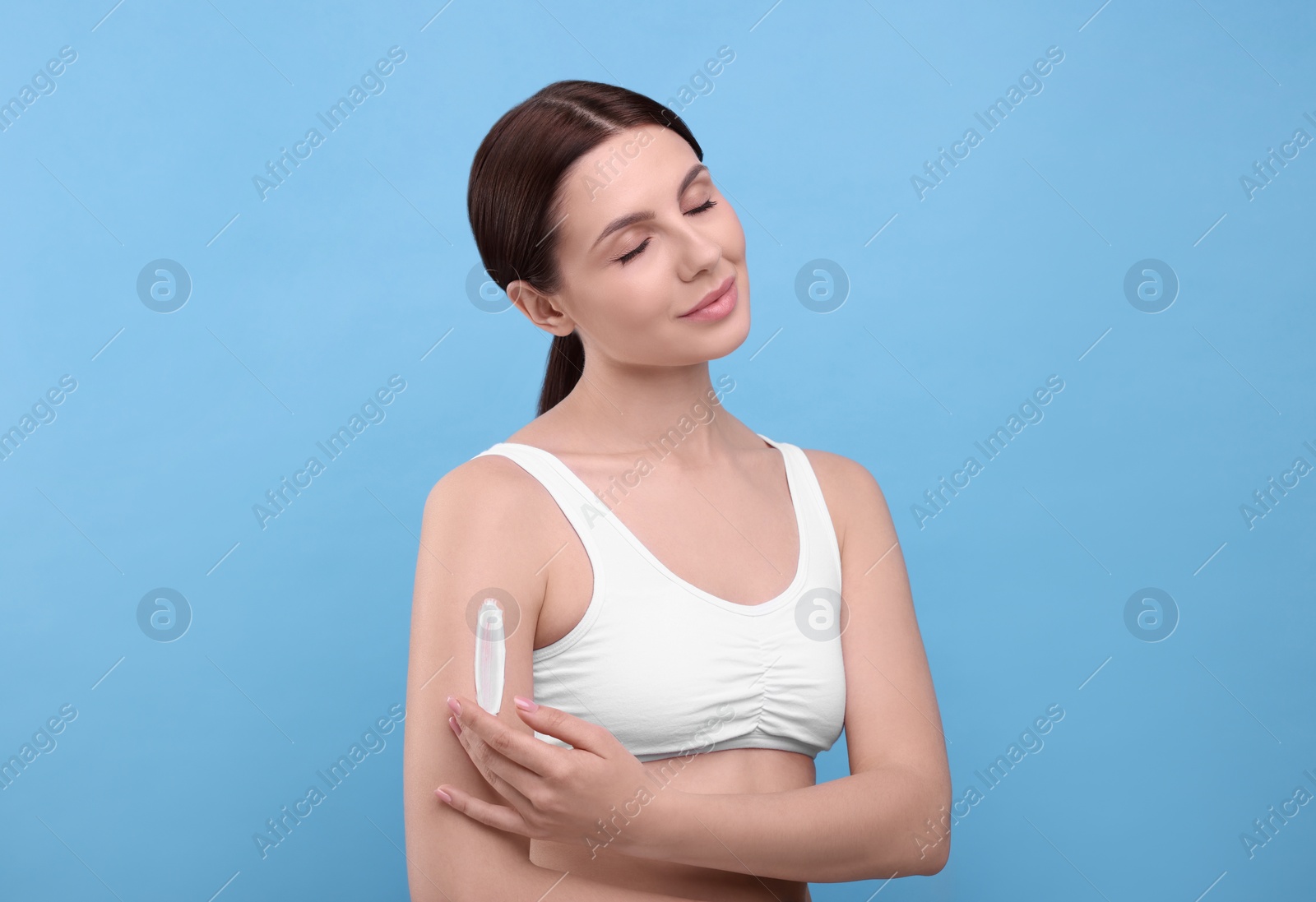 Photo of Beautiful woman with smear of body cream on her arm against light blue background