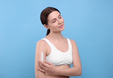 Beautiful woman with smear of body cream on her arm against light blue background