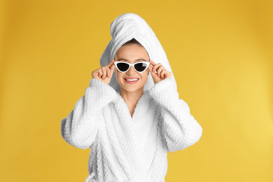 Beautiful young woman in bathrobe and sunglasses on yellow background