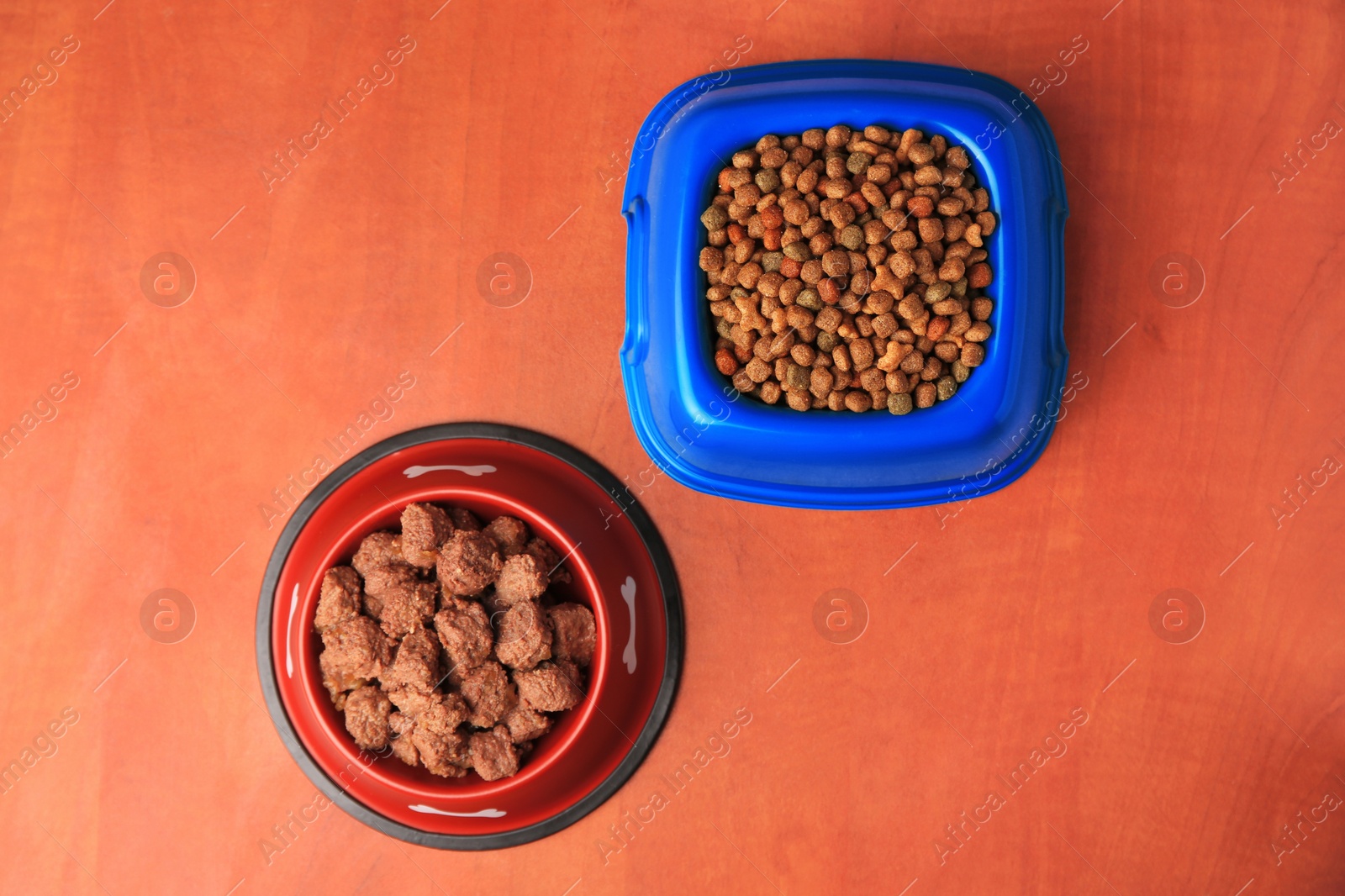 Photo of Dry and wet pet food in feeding bowls on orange background, flat lay