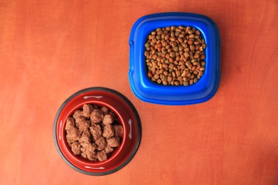 Photo of Dry and wet pet food in feeding bowls on orange background, flat lay