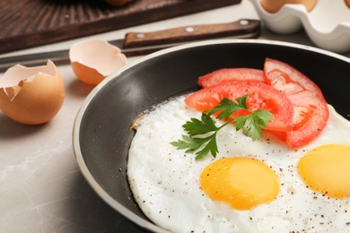 Photo of Pan with fried sunny side up eggs and tomato on table, closeup