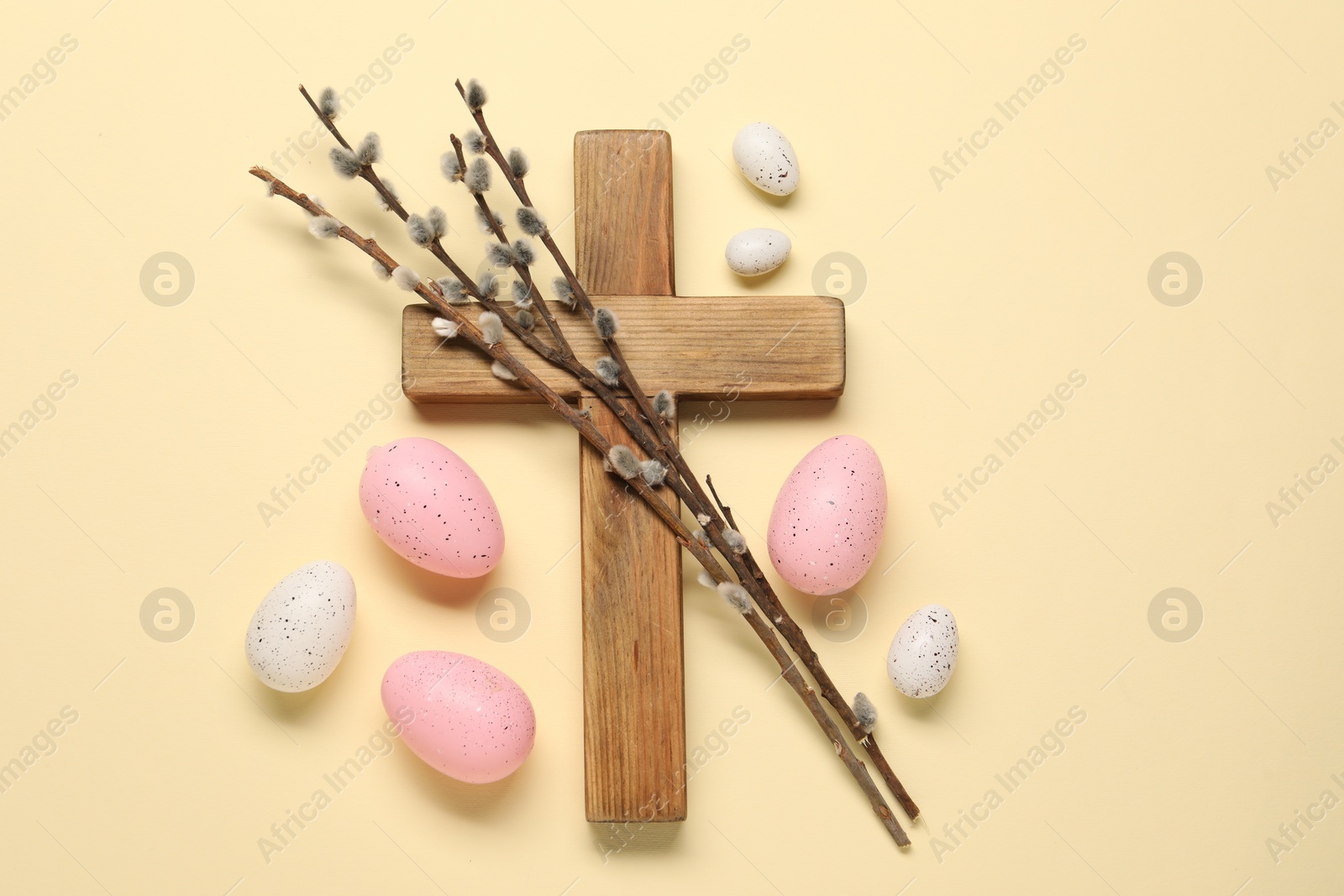 Photo of Wooden cross, painted Easter eggs and willow branches on beige background, flat lay