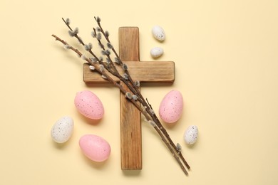 Wooden cross, painted Easter eggs and willow branches on beige background, flat lay