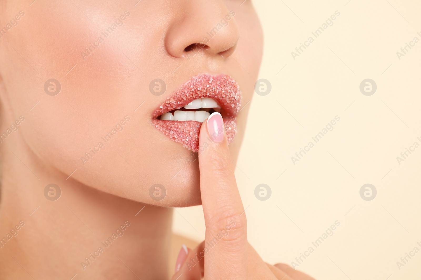 Photo of Young woman with sugar scrub on lips against beige background, closeup