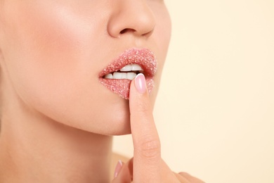 Young woman with sugar scrub on lips against beige background, closeup