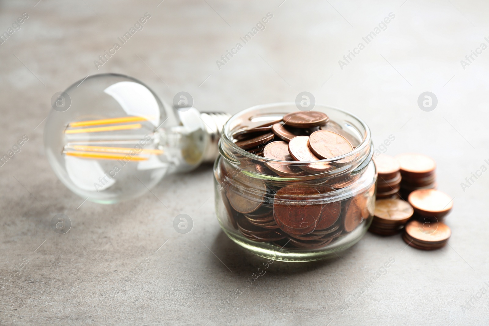 Photo of Glass jar, coins and light bulb on grey background