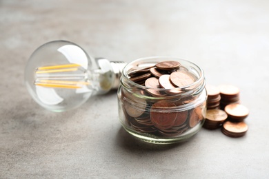 Glass jar, coins and light bulb on grey background