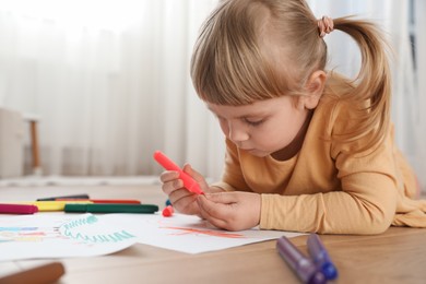 Photo of Cute little girl drawing with marker on floor indoors. Child`s art