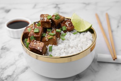 Photo of Bowl of rice with fried tofu and green onions on white marble table, closeup