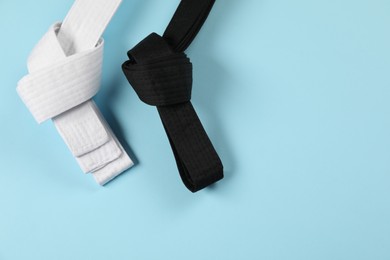White and black karate belts on light blue background, flat lay. Space for text