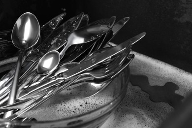 Washing silver spoons, forks and knives in kitchen sink with foam. Space for text