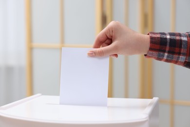 Photo of Woman putting her vote into ballot box on blurred background, closeup