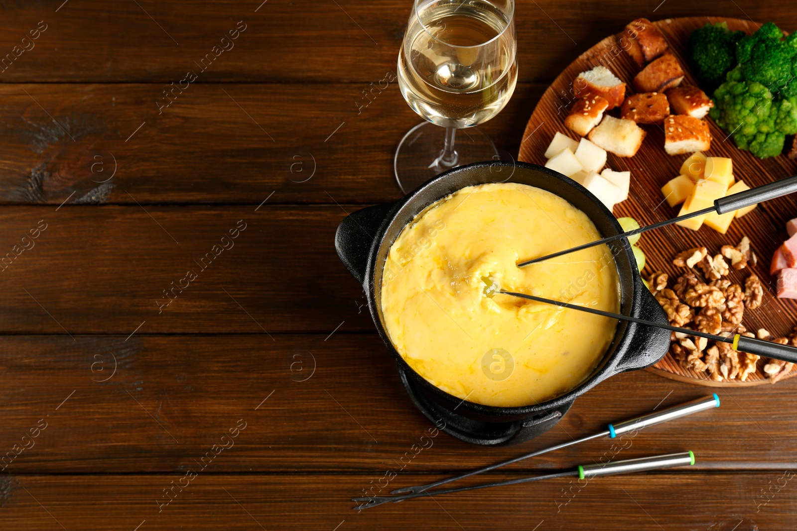 Photo of Fondue pot with melted cheese, glass of wine and different products on wooden table, flat lay. Space for text