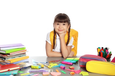 Cute girl sitting at table with school stationery against white background