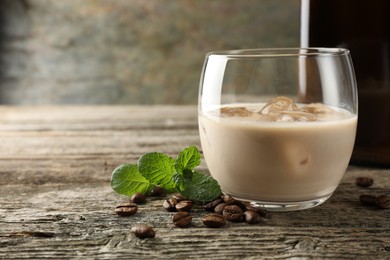Photo of Coffee cream liqueur in glass, mint and beans on wooden table, closeup. Space for text