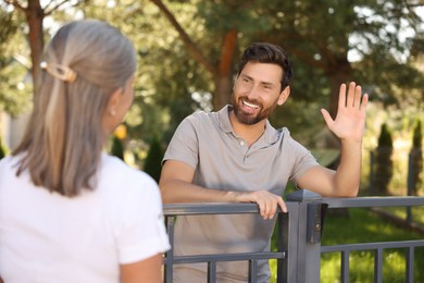 Photo of Friendly relationship with neighbours. Happy man greeting senior woman near fence outdoors