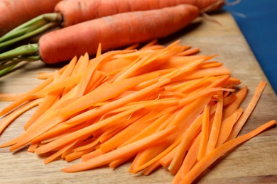 Photo of Fresh ripe juicy carrot sticks and whole vegetables on wooden board, closeup