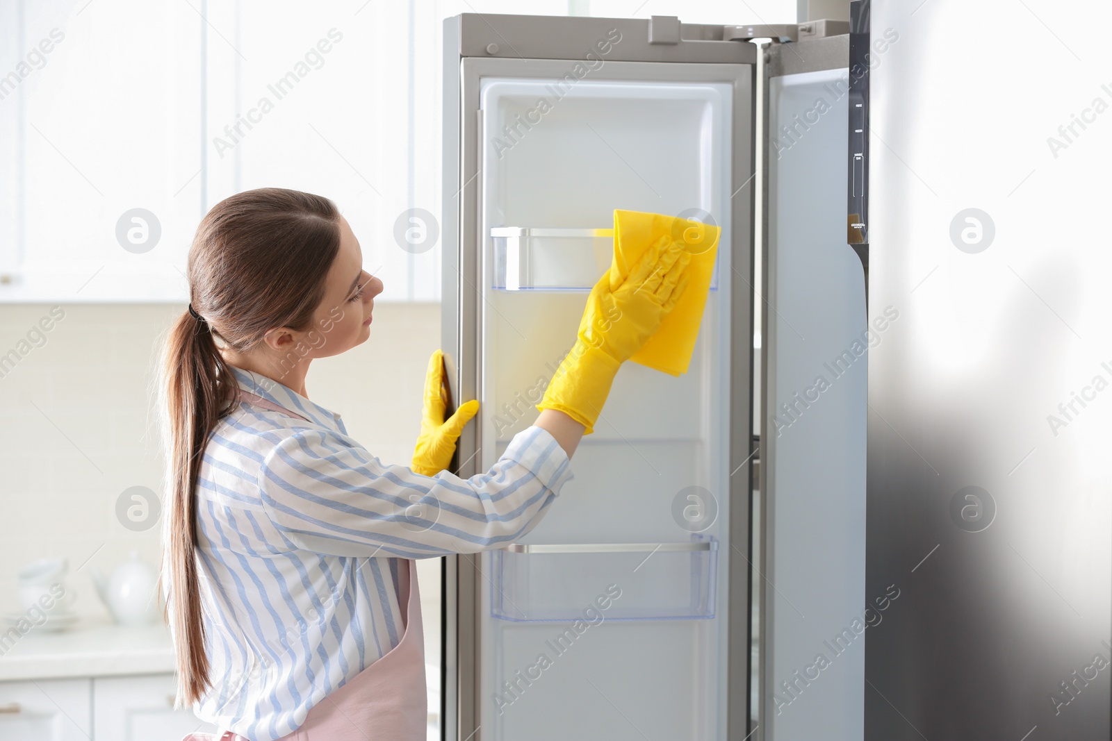 Photo of Woman in rubber gloves cleaning refrigerator at home