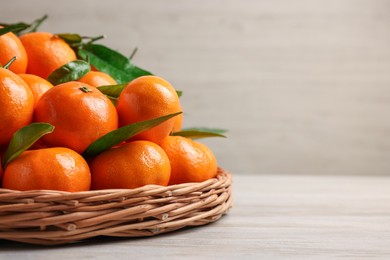 Fresh ripe juicy tangerines and green leaves on white wooden table, closeup with space for text