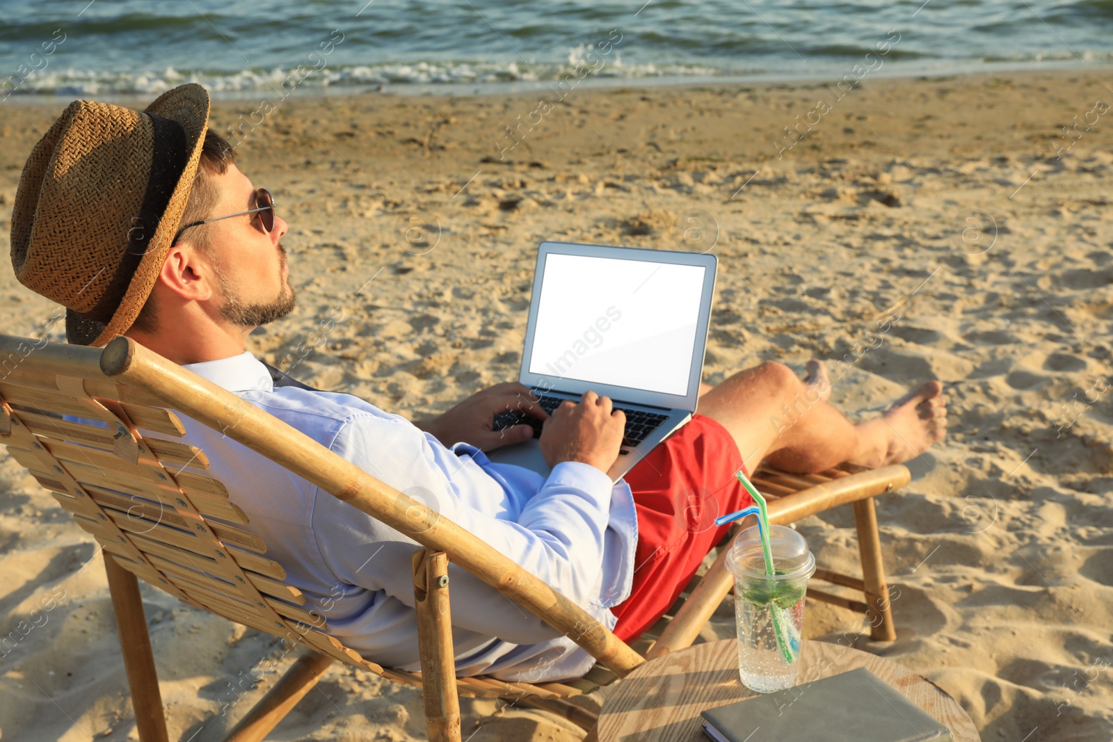 Photo of Man with laptop sitting on sandy beach. Business trip