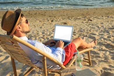 Photo of Man with laptop sitting on sandy beach. Business trip