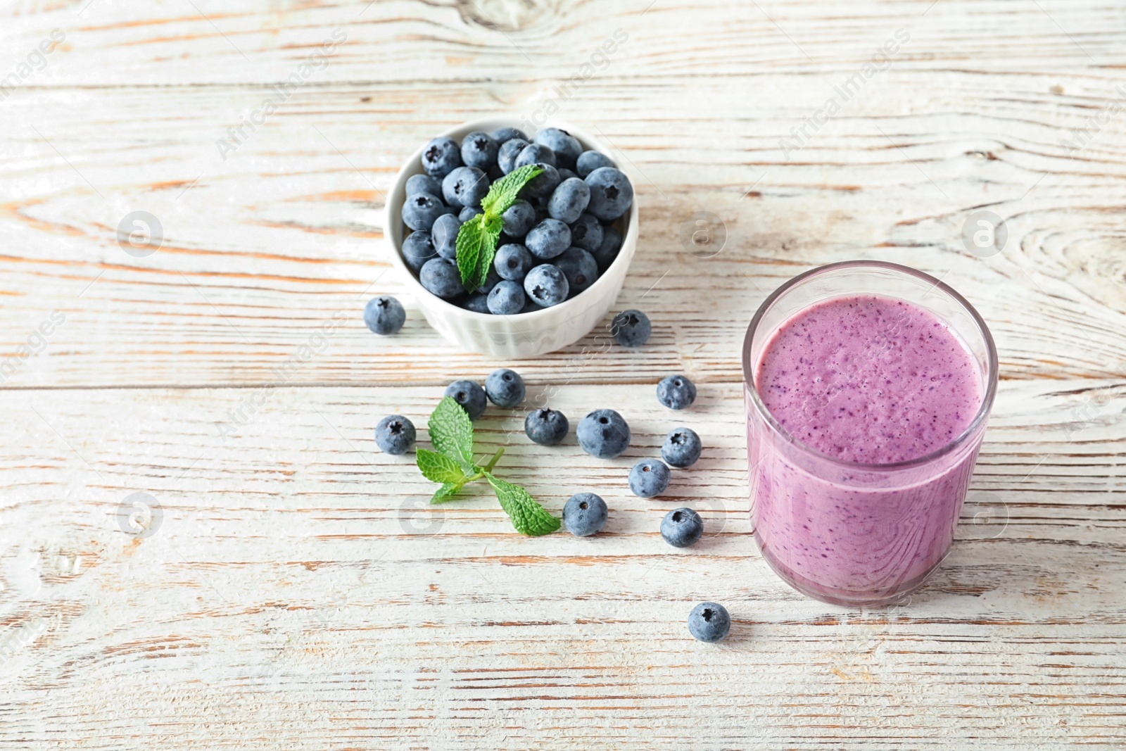 Photo of Tasty blueberry smoothie in glass and bowl with fresh berries on wooden table