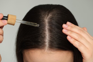 Woman applying essential oil onto hair on grey background, closeup