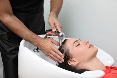 Professional hairdresser washing client's hair at sink indoors, closeup