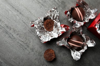 Many different delicious chocolate truffles with wrappers on grey table, flat lay. Space for text