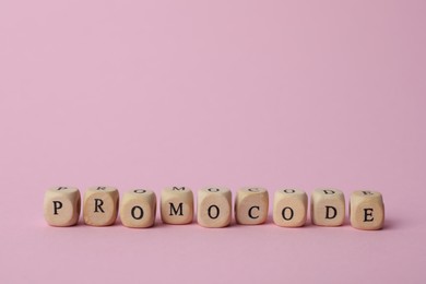 Photo of Word Promocode made of wooden cubes with letters on pink background, space for text