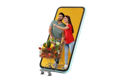 Image of Grocery shopping via internet. Happy couple with shopping cart full of products walking out of huge smartphone on white background