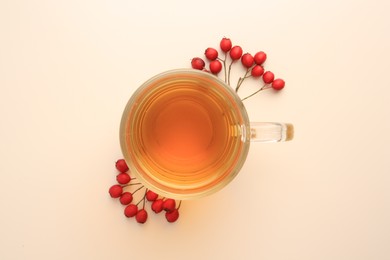Photo of Cup with hawthorn tea and berries on beige table, top view