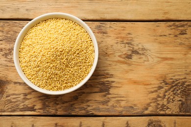 Photo of Millet groats in bowl on wooden table, top view. Space for text