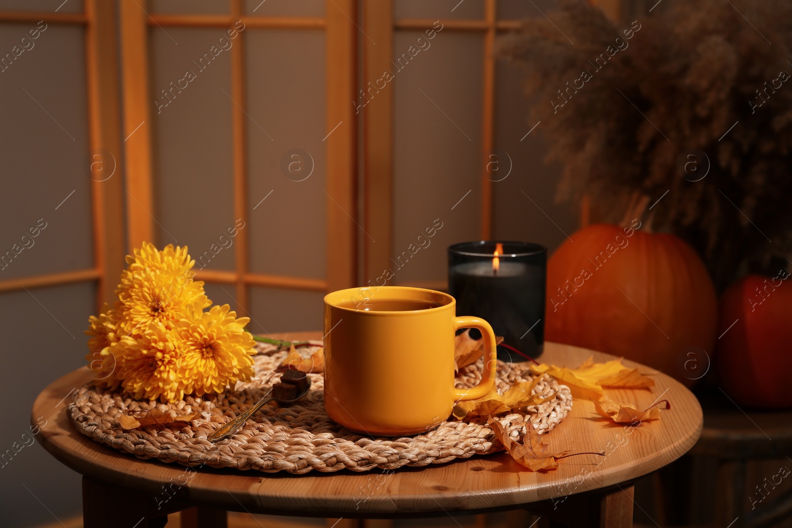 Photo of Cup of aromatic tea, beautiful flowers, candle and autumn leaves on wooden table indoors