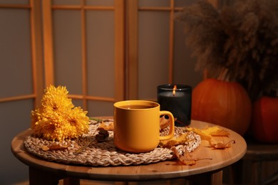 Cup of aromatic tea, beautiful flowers, candle and autumn leaves on wooden table indoors