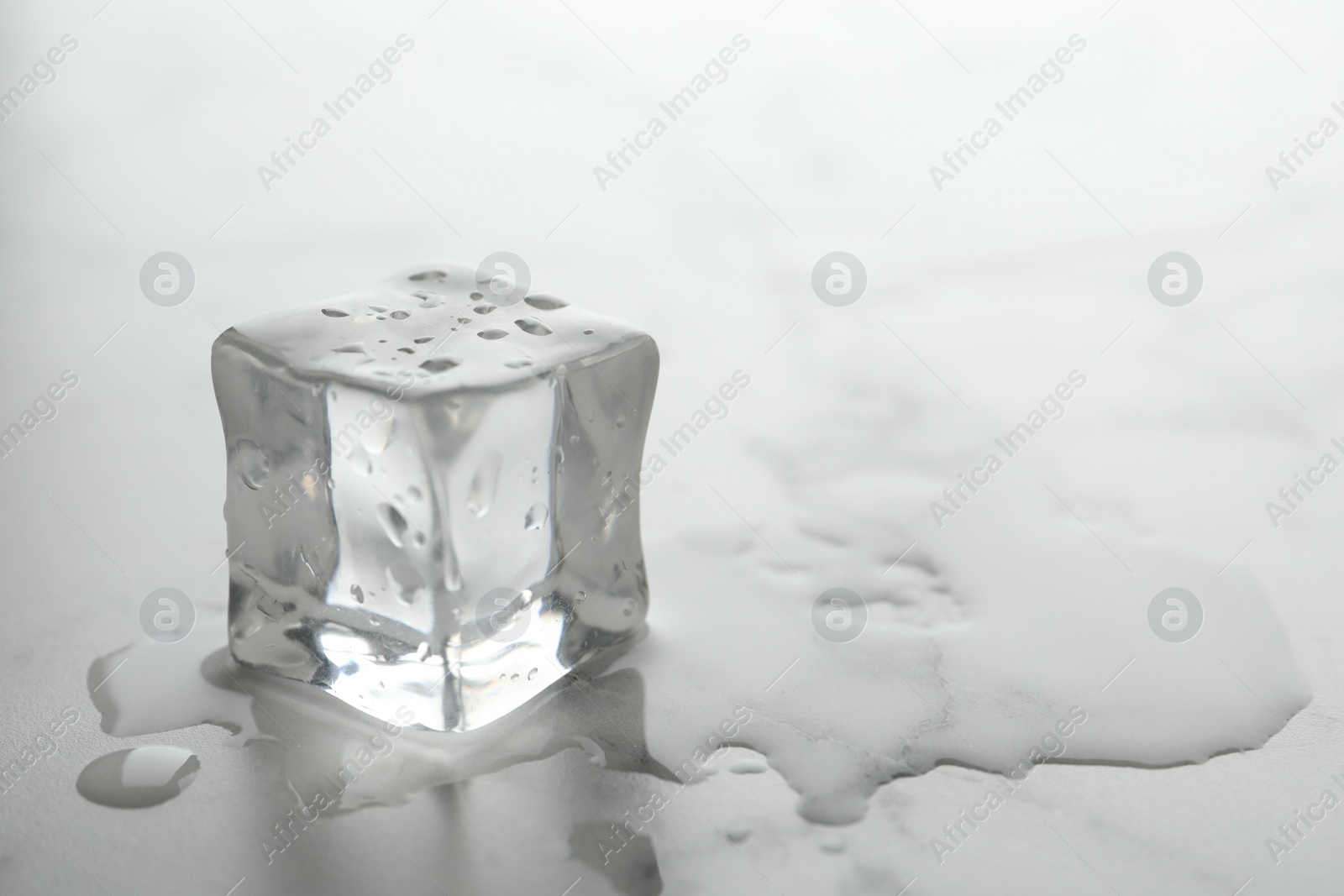 Photo of Wet ice cube on white table, closeup. Space for text