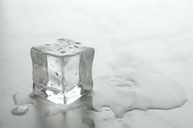 Wet ice cube on white table, closeup. Space for text