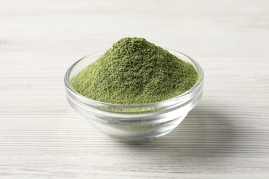 Photo of Wheat grass powder in glass bowl on white wooden table, closeup