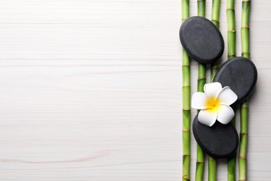 Spa stones, bamboo stems and plumeria flower on light wooden table, flat lay. Space for text