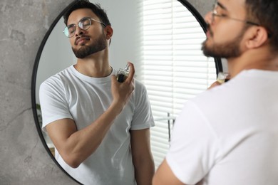 Photo of Man spraying luxury perfume near mirror indoors