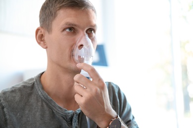 Photo of Young man using asthma machine indoors. Space for text