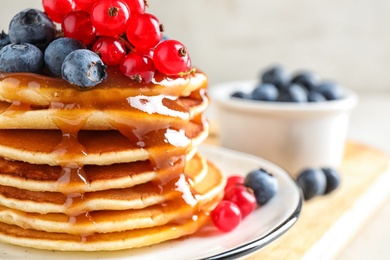 Photo of Delicious pancakes with fresh berries and syrup on table, closeup