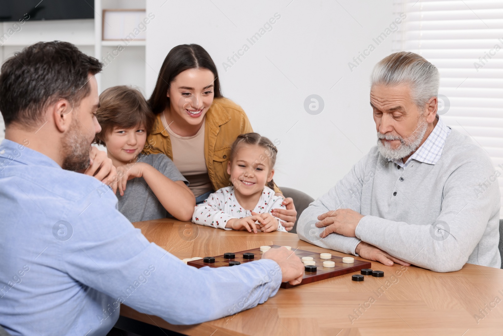 Photo of Happy family playing checkers at table in room